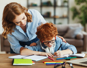 Mother helping child with homework, looks at her son's notebook at home.