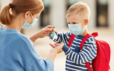 Mother disinfecting hands of schoolboy.