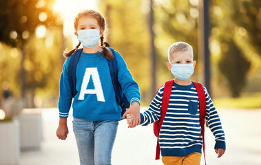 Cheerful siblings in protective masks with school backpacks.