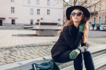 Stylish woman wearing hat, glasses with green handbag and gloves outdoors. Autumn clothes, accessories. Female fashion.