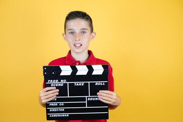 Young beautiful child boy over isolated yellow background holding clapperboard very happy