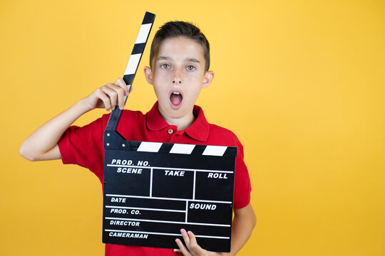 Young beautiful child boy over isolated yellow background holding clapperboard very happy having fun