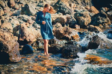 Woman in blue dress walking on coastline. Sharp rocky terrain. Meditation and health. Seascape and relaxation concept