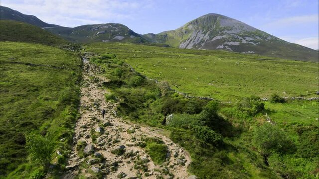 Panning aerial, woman hikes up Ireland mountain