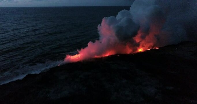 Slow motion aerial, lava flows into ocean at night