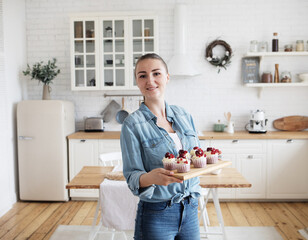 Young baker woman holding cupcakes. Happy, smiling and cheerful.