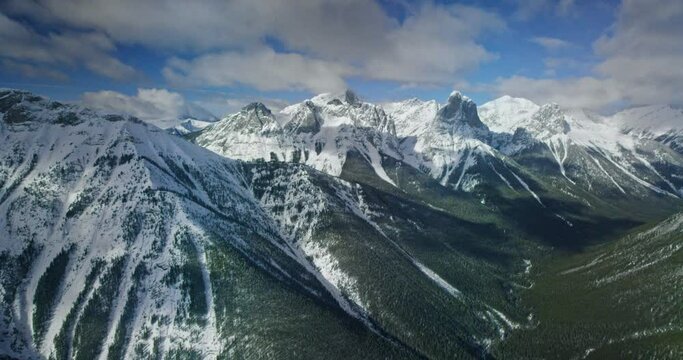 Helicopter flies over snowy mountain landscape in Banff National Park, wide aerial