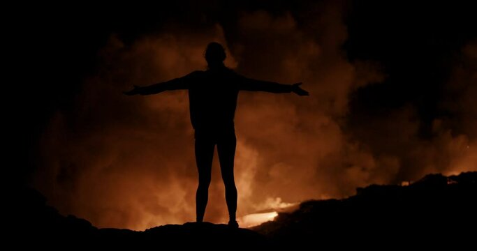 Silhouetted woman stands in front of lava flow at night, wide