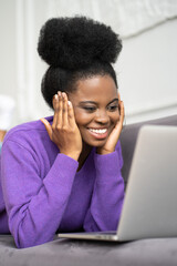 Smiling African American millennial woman with afro hairstyle wear purple sweater lying on sofa,...