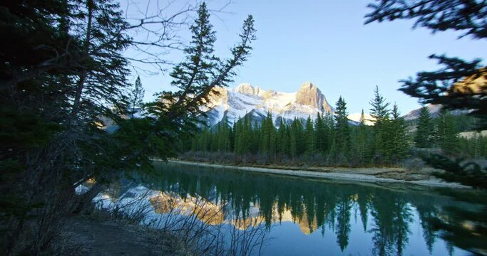 Pan right, mountains tower over creek in Banff National Park