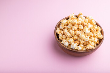 Popcorn with caramel in wooden bowl on a pastel pink background. Side view, copy space.