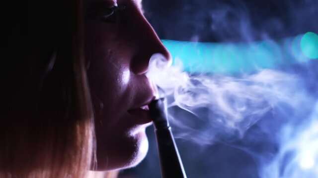Nightlife concept, beautiful young woman profile smoking hookah. Media. Close up side view of a girl face vaping in nightclub, exhaling smoke at the party.