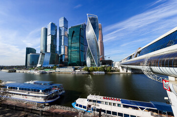 Skyscrapers, modern business office buildings in commercial district with river, bridge, tourist boats, ships, blue sky and white clouds on background 