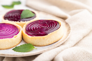 Sweet tartlets with jelly and milk cream with cup of coffee on a white wooden background. Side view, selective focus.