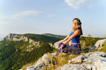 Side view on caucasian woman sitting on the cliff on the top of the mountain in lotus yoga position in summer or autumn day - Meditation and relaxation spirituality concept copy space