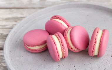 Closeup view of pink macarons filled with vanilla cream on the grey plate.