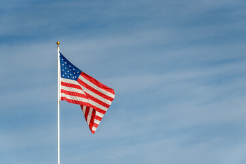 American flag blowing in the wind at sunset, against a blue sky with wispy white clouds
