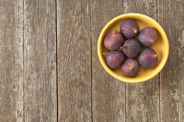 Fresh figs in a wooden bowl on a rustic background, top view.