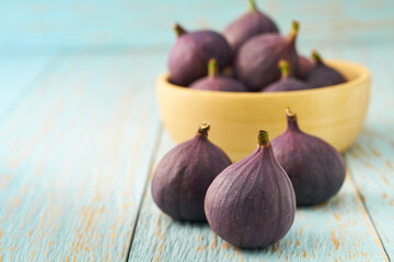 Fresh figs in a wooden bowl on a blue table with copy space.