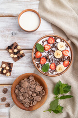 Chocolate cornflakes with milk and strawberry in wooden bowl on white wooden background. Top view.