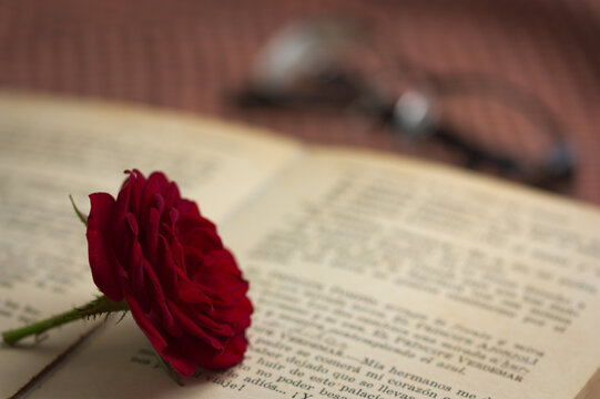 A red rose on an old book next to some glasses