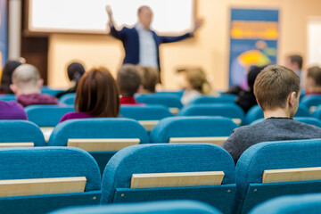 People At Conference Listening to Presenter In Front of a Group of Listeneres in the Hall. Standing in Front of The Big Screen.