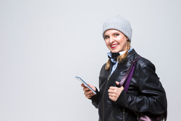 Smiling Happy Caucasian Blond Girl in Warm Hat and Leather Jacket With Cellphone and Backpack.