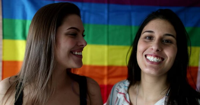 Portrait of two women looking at camera with rainbow flag LGBT symbol in background