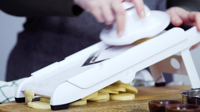 Time lapse. Slicing organic gold potatoes on a V-blade mandoline to prepare scalloped potatoes.