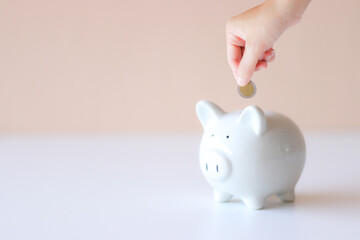 Saving piggy bank white pig on the floor It has a light pink background and a hand in charge of coin. Convey to savings