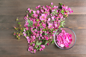 rose petals in a glass bowl on the background of lying pink flowers for drying on wood table. flat...