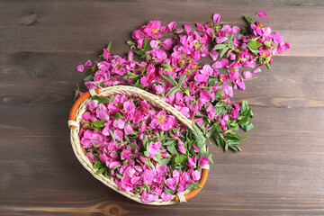 wicker basket with rose petals and flowers in pink on a wooden background. top view.