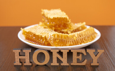 Honeycombs in white plate on the wooden table. Natural organic bee product. Healthy lifestyle. Word honey. Close-up photo
