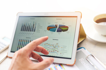 Business graphs chart on a tablet computer technology on the table with coffee cup on desk and...