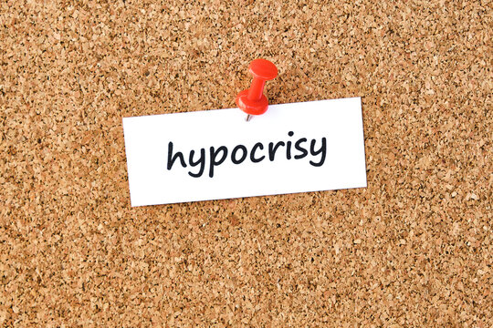 Hypocrisy. Word written on a piece of paper, cork board background.