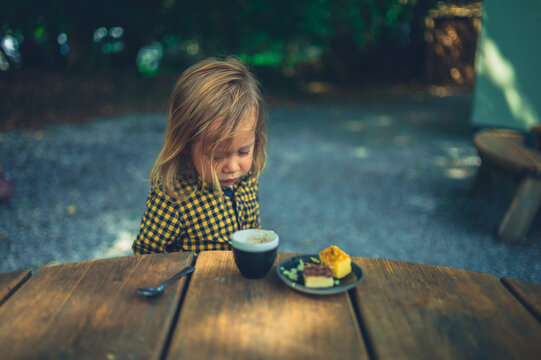Preschooler drinking coffee and eating cake in outdoor cafe