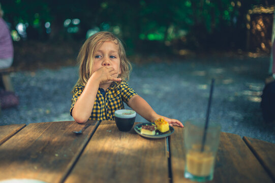 Preschooler drinking coffee and eating cake in outdoor cafe