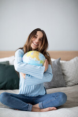 Cheerful young woman hugging globe sitting on the couch at home.