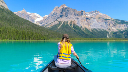 Emerald Lake Canoeing. The view on the back of woman in yellow life jacket paddling from canoe on...