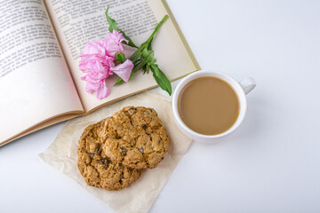 Coffee or tea with milk and oat cookies. Reading old book and snack in spring, summer day in garden. Romantic vintage still life with pink flowers.