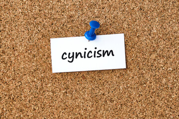 Cynicism. Word written on a piece of paper, cork board background.