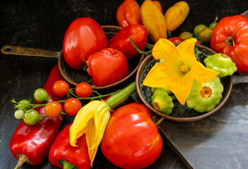Harvest of fresh farm vegetables on copper pans  - tomatoes, red pepper, squashes, and in on a black background. Fresh vegetarian food concept