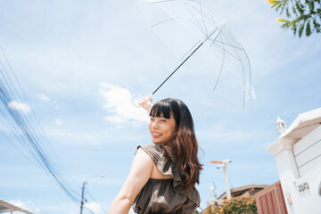 Asian woman traveler holding transparent umbrella outdoors in sunny day.
