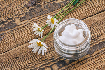 Cosmetic cream and fresh chamomile flowers on wooden background.