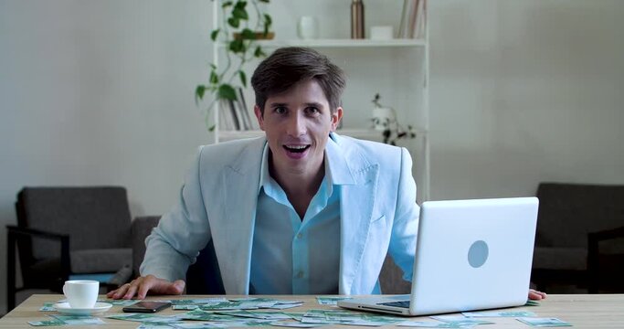 Funny comic business men office worker sitting at table in front of mountain of money, grabbing hold of dollar banknotes with his teeth like wild animal, comical celebrating successful investment