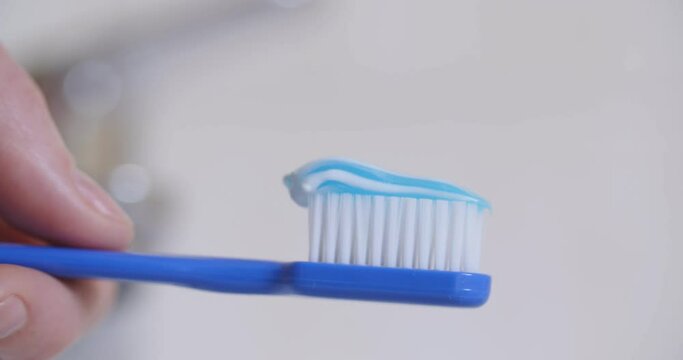 Closeup shot of a woman squeezing toothpaste onto a toothbrush.