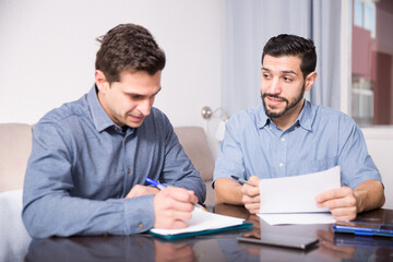 Two smiling friends discussing papers while sitting at table at home