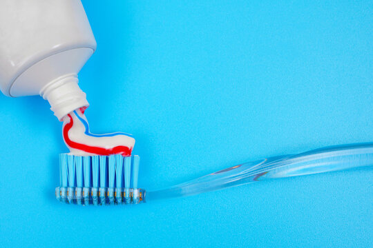 putting toothpaste on toothbrush on blue background with copy space