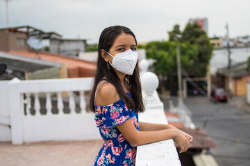 Ni&ntilde;a latina con protecci&oacute;n mascarilla pensando desde su balc&oacute;n