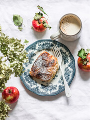 Piece of apple strudel and coffee with cream on a light background, top view. Delicious breakfast, dessert